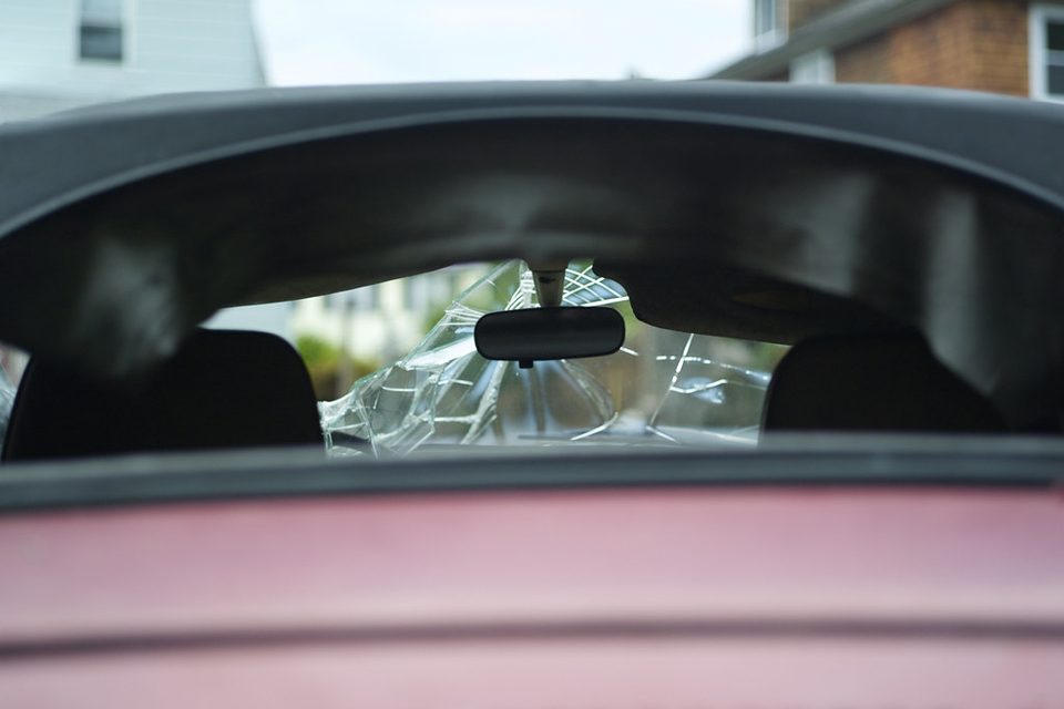 A shattered laminated windscreen seen from inside a car, hairline cracks webbing out across the glass